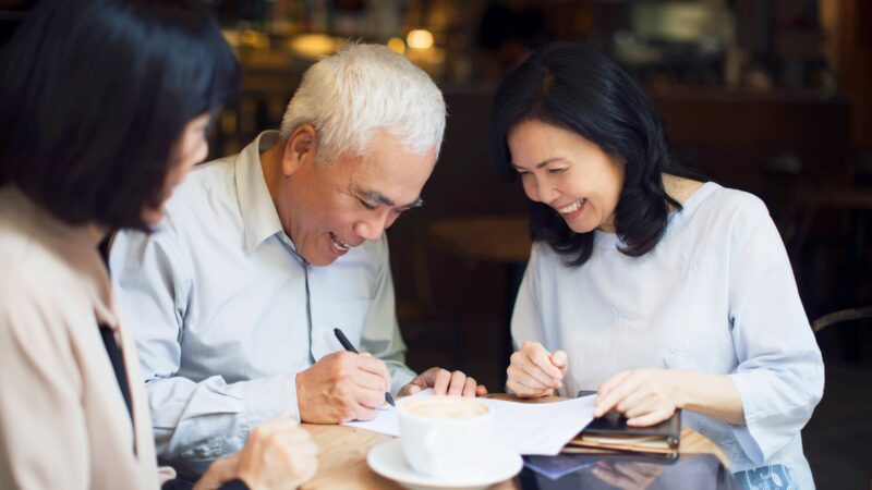 Older couple sitting side by side signing documents together