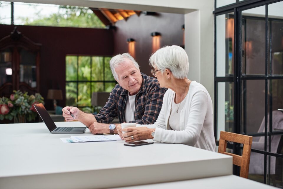 Older man and woman at a table looking at a laptop together