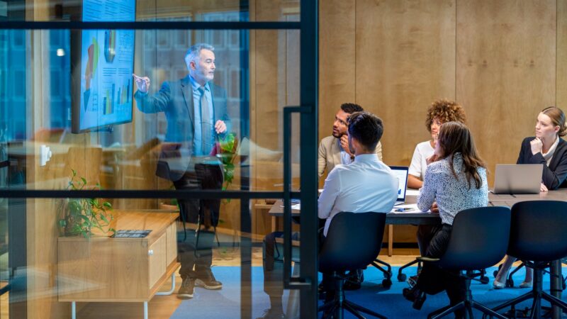 Two businesspeople in suits shaking hands through a glass wall in an office lobby