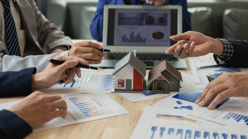 Hands around a table with charts and documents, one person pointing at data