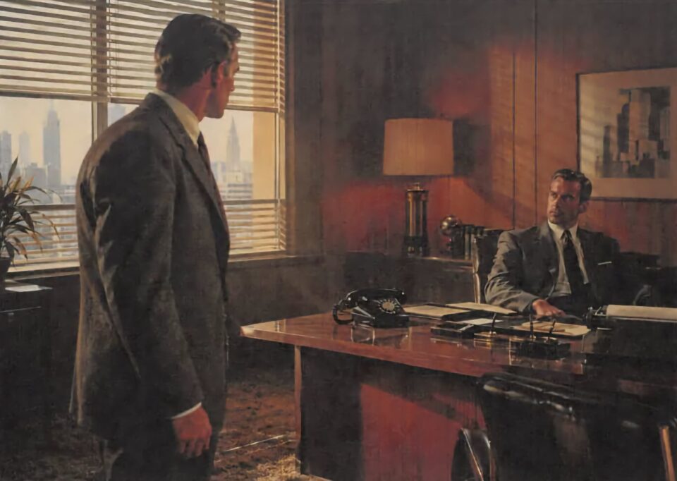 Two men in suits facing each other across an executive desk in a wood-paneled office